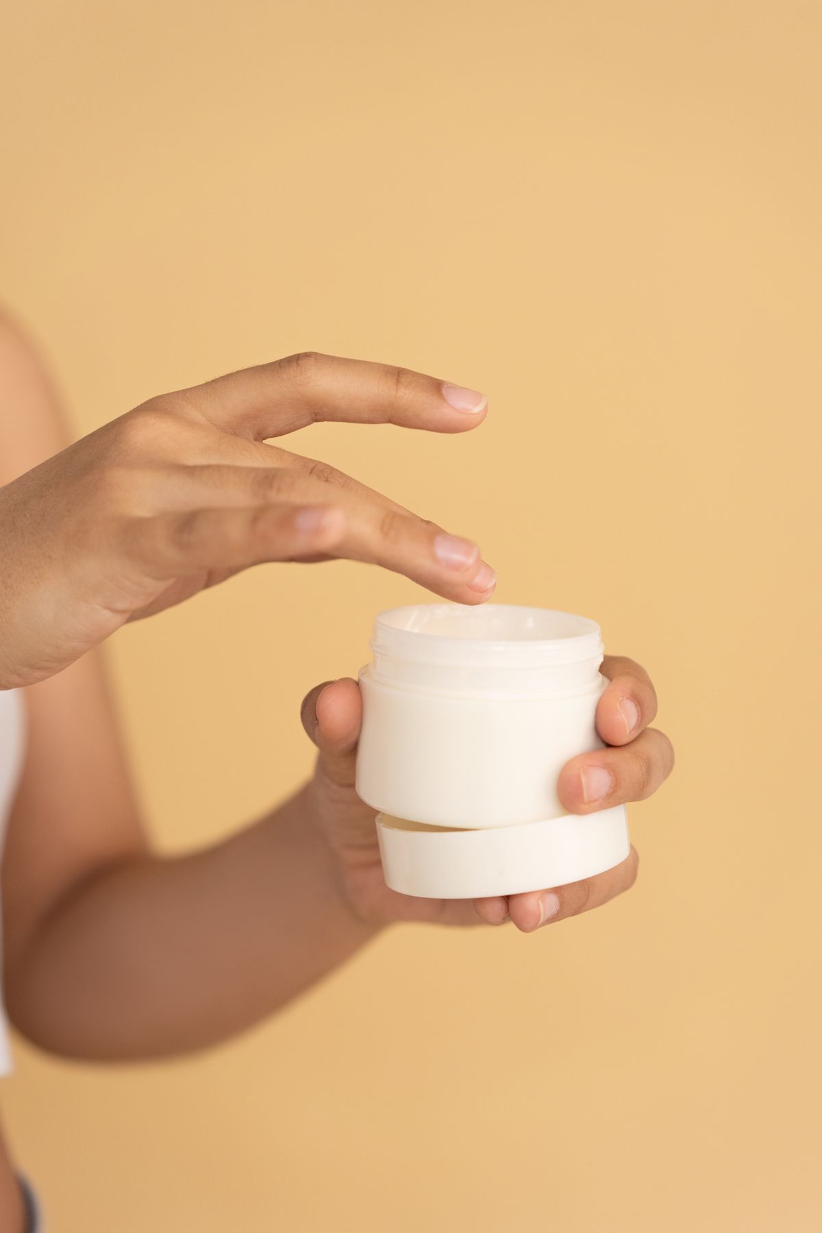 Hands holding a skincare jar against an orange background
